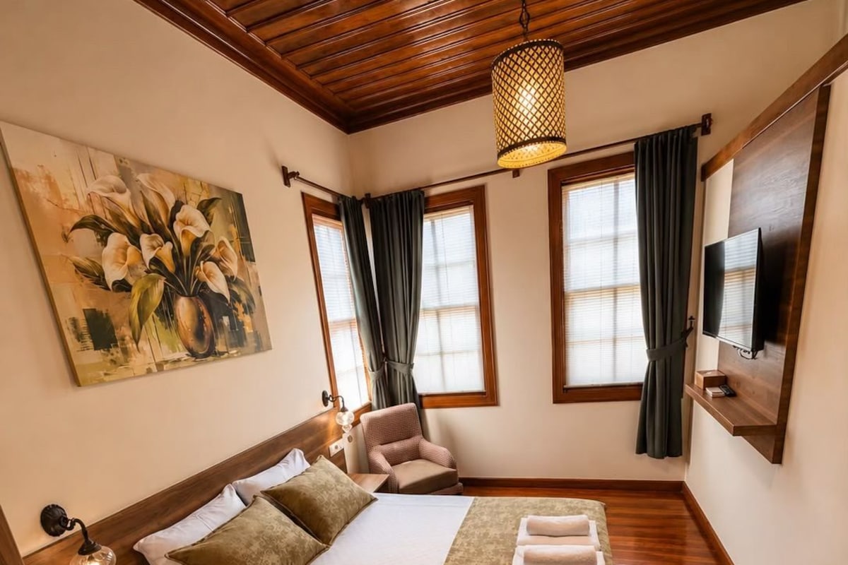 Ein Schlafzimmer mit Holzboden, einem Bett mit grüner Tagesdecke, einem Gemälde an der Wand und einem an der Wand befestigten Fernseher.