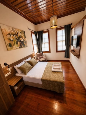 Ein Schlafzimmer mit Holzboden, einem Bett mit grüner Tagesdecke, einem Gemälde an der Wand und einem an der Wand befestigten Fernseher.