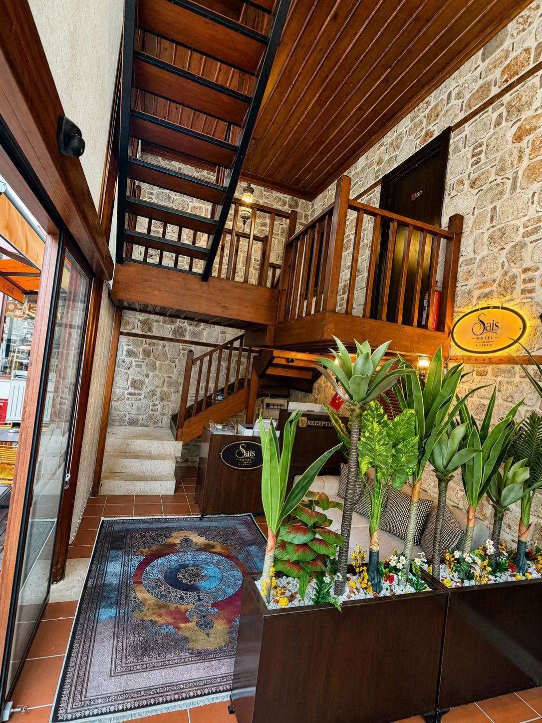Vestíbulo de hotel con escalera, mostrador de recepción y cartelera informativa.