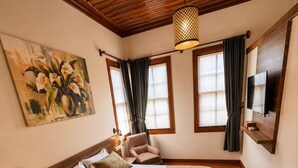 A bedroom with a wooden ceiling, a bed with a green bedspread, a painting on the wall, and a TV mounted on the wall. - Sais Hotel Kaleiçi (Antalya)