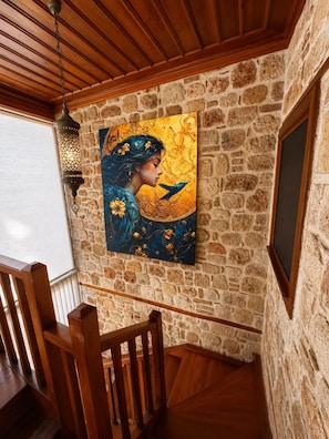 A staircase with a stone wall and a painting of a woman with a bird. - Sais Hotel Kaleiçi (Antalya)