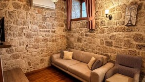 A cozy room with a stone wall, wooden floor, a sofa, a chair, a small table, and a wall-mounted lamp. - Sais Hotel Kaleiçi (Antalya)