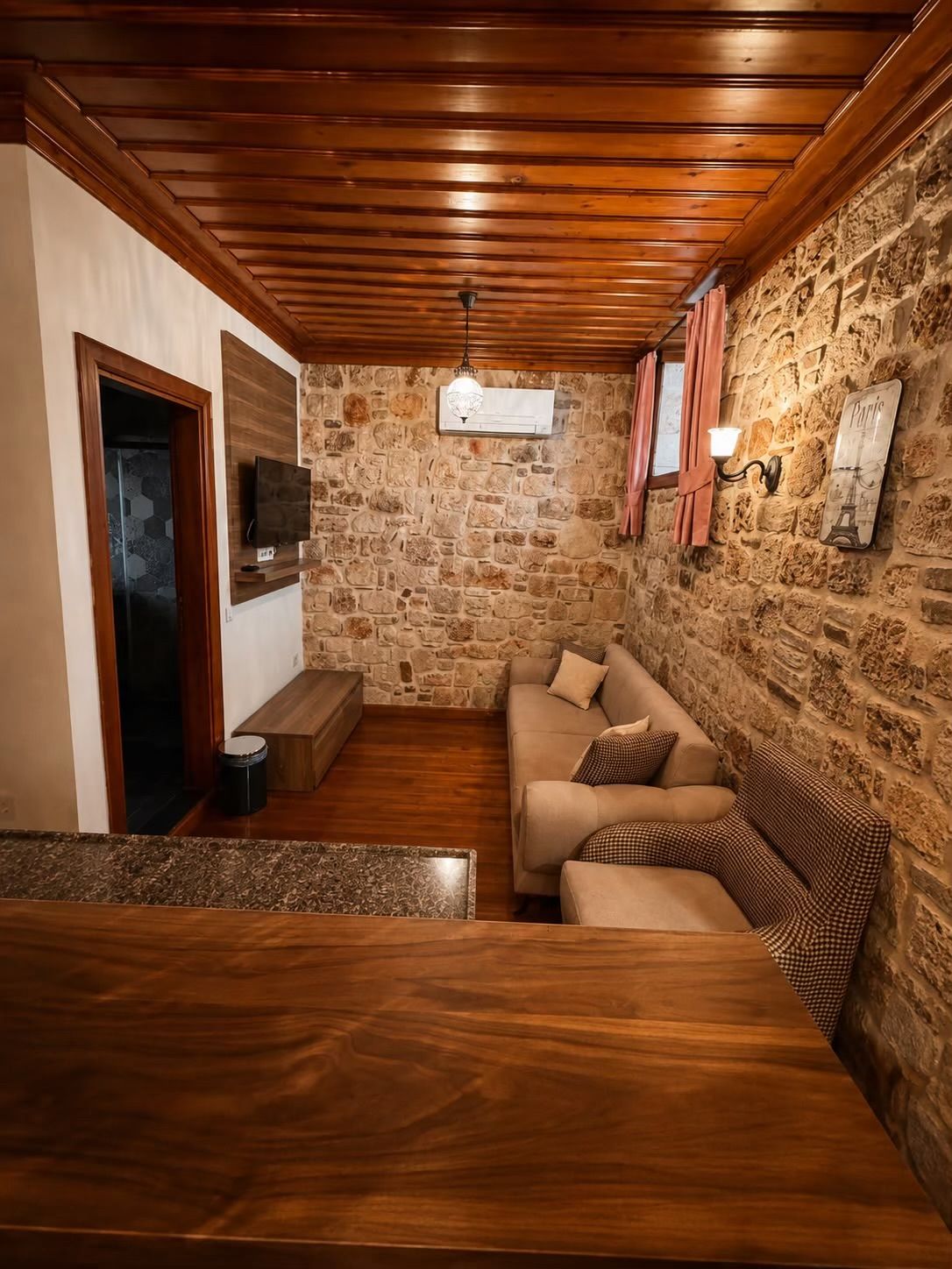 Una habitación acogedora con pared de piedra, techo de madera, un sofá y un banco.