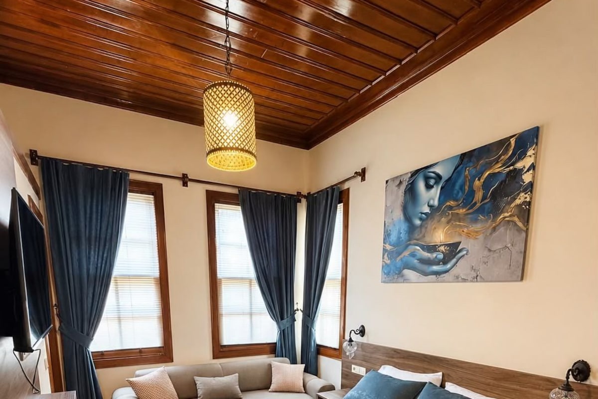 A bedroom with a large bed, a sofa, a TV, and a painting on the wall.