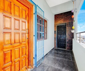 A hallway with a wooden door, a blue-framed window, and a black door with a metal grille. - Deluxe With Balcony (Tirupati)