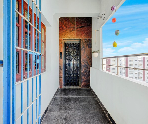 A narrow hallway with a black metal gate door, a blue and red window, and a view of buildings in the background.