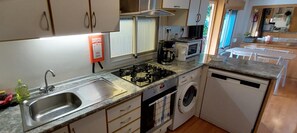 A compact kitchen with a gas stove, microwave, sink, and a washing machine. - 🌊 Fully equipped mobile home for 4 people – SIBLU Mimizan Plage (Mimizan)