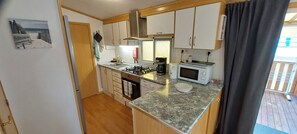 A compact kitchen with a gas stove, microwave, and a coffee maker. - 🌊 Fully equipped mobile home for 4 people – SIBLU Mimizan Plage (Mimizan)