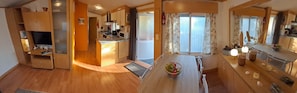 A modern kitchen with wooden cabinets, a built-in microwave, and a dining area with a wooden table and chairs. - 🌊 Fully equipped mobile home for 4 people – SIBLU Mimizan Plage (Mimizan)
