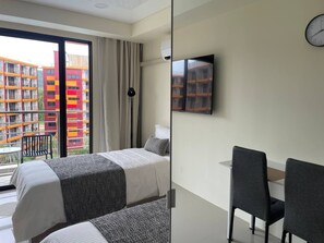 A hotel room with a bed, a desk, a chair, a TV, and a view of colorful buildings. - Studio apartment in tranquil Tambon Mai Khao with AC (Tambon Mai Khao)