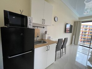 A modern kitchen with a refrigerator, microwave, and sink. There is a dining area with chairs and a television mounted on the wall. - Studio apartment in tranquil Tambon Mai Khao with AC (Tambon Mai Khao)
