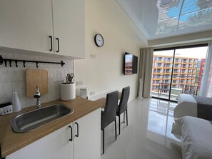 A modern hotel room with a kitchen area, a dining table with chairs, a bed, and a balcony with a view of a building. - Studio apartment in tranquil Tambon Mai Khao with AC (Tambon Mai Khao)
