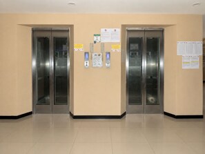 Un espace ascenseur propre et moderne, doté de deux ascenseurs, de panneaux de commande et de panneaux d’information fixés aux murs.