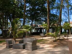 Un espace extérieur aménagé avec des meubles en osier, entouré d’arbres et avec un bâtiment visible au loin.