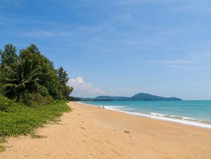 Ein Strand mit blauem Himmel, sandigem Ufer und einer fernen Bergkette.