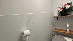 A bathroom with a toilet, sink, and a shelf with a bottle and flowers. - Charming Apartment in Center of Lier (Lier)