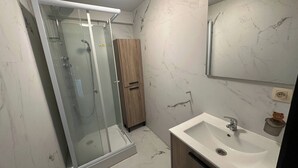 A bathroom with a glass-enclosed shower, a wooden cabinet, a sink with a mirror, and marble-patterned walls. - Charming Apartment in Center of Lier (Lier)