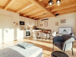 Une cuisine moderne avec des meubles blancs, un coin repas doté d’une table et de chaises en bois, et un téléviseur affichant le mot « REHFGIUM ».