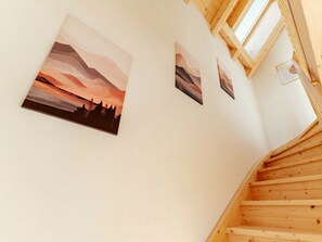 Un escalier en bois mène à un palier où sont accrochées trois œuvres d’art encadrées au mur.