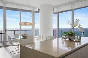 Ein moderner Essbereich mit einem Glastisch, weißen Stühlen und einem großen Fenster mit Meerblick.