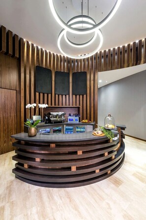 A reception desk with a modern design, featuring a wooden panel wall, a circular light fixture, and a bar area with a coffee machine and a display case. - 29th Floor Double Oceanfront Condo Side by Side (Hollywood)