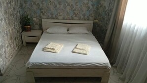 A bed with a white mattress and wooden frame, a nightstand with a plant, and a window with curtains. - Veni Vedi guesthouse  (Vedi)