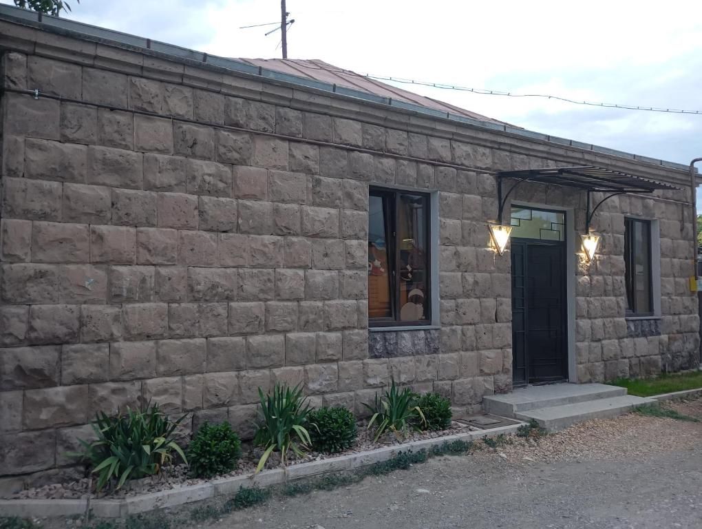 Un edificio de piedra con techo de metal, una puerta negra y un pequeño porche con plantas.