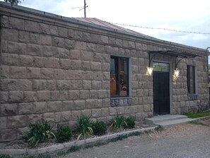 Un edificio de piedra con techo de metal, una puerta negra y un pequeño porche con plantas.