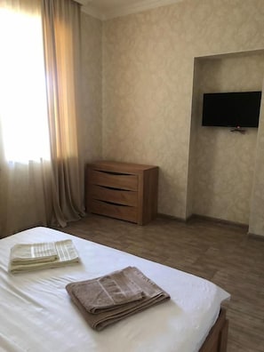 A hotel room with a bed, a wooden dresser, a flat-screen TV mounted on the wall, and a window with curtains. - Veni Vedi guesthouse  (Vedi)