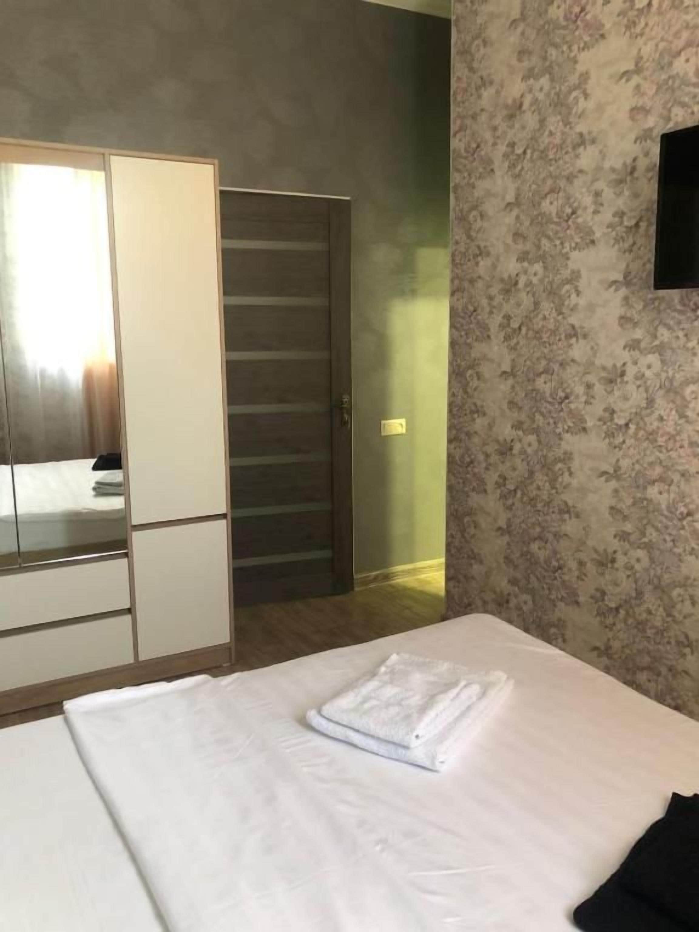 A bedroom with a bed, a wardrobe, a door, and a wall with a floral pattern.