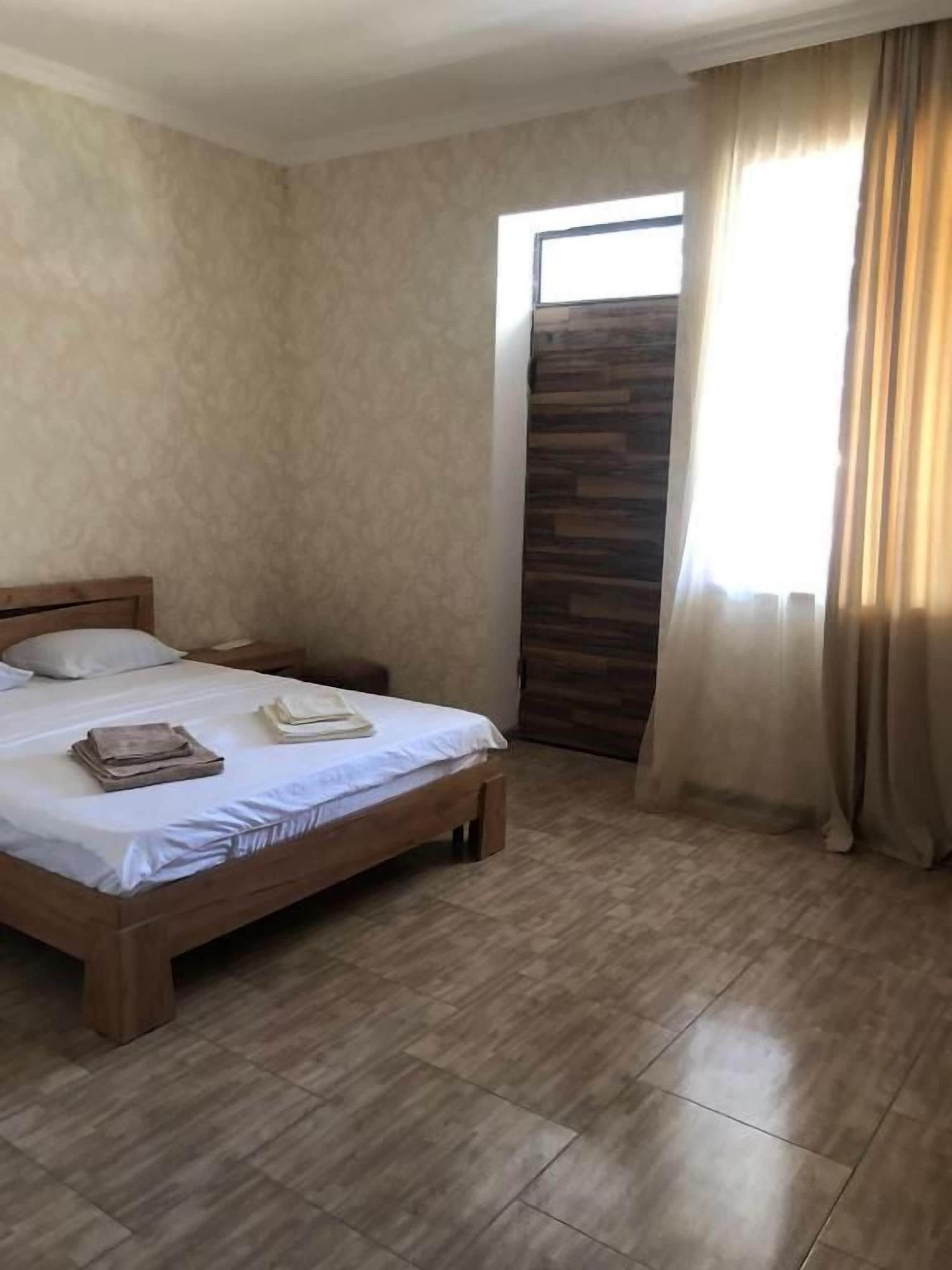 Un dormitorio con una cama, una mesita de noche, una ventana con cortinas y una puerta con un panel de madera.