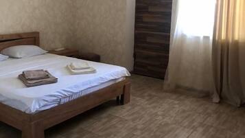 Un dormitorio con una cama, una mesita de noche, una ventana con cortinas y una puerta con un panel de madera.