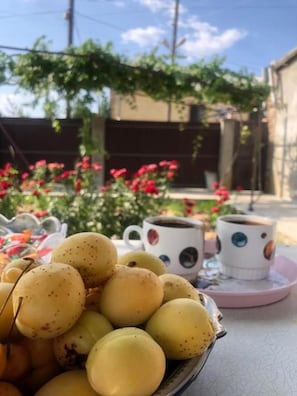 A table with a bowl of yellow fruits, two white cups with colorful patterns, and a pink saucer. - Veni Vedi guesthouse  (Vedi)