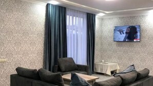 A living room with a sectional sofa, a flat-screen TV mounted on the wall, and a window with curtains. - Veni Vedi guesthouse  (Vedi)