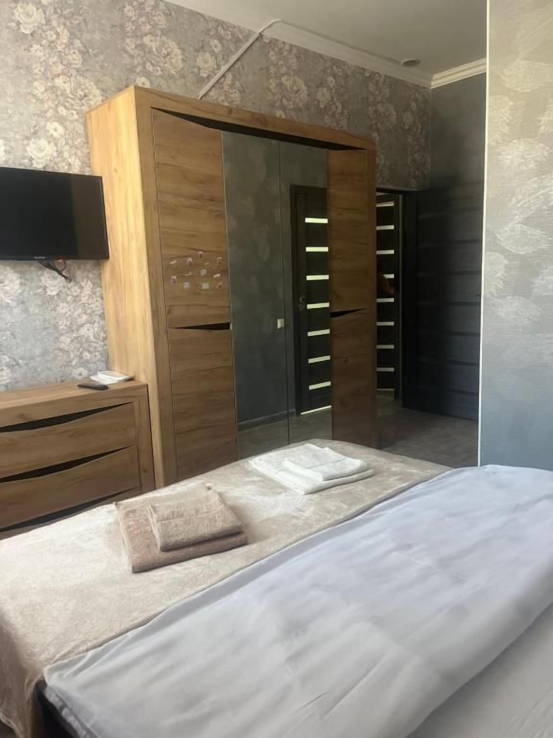 Un dormitorio con una cama, un armario de madera, un televisor y un espejo.