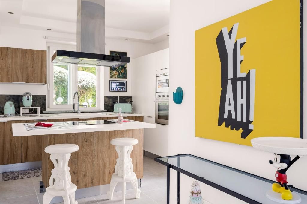 A modern kitchen with a central island, bar stools, and a large yellow artwork.