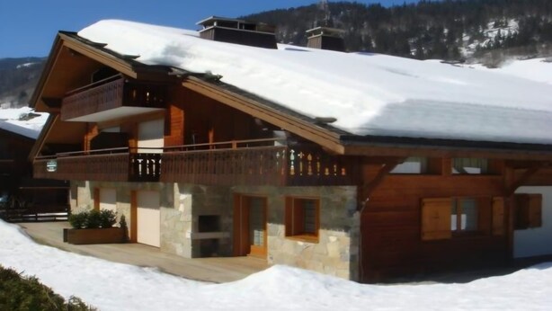 Eine Holzhütte mit Balkon, Steinwänden und einem mit Schnee bedeckten Dach.
