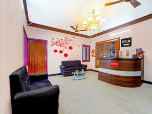 A hotel reception area with a reception desk, a sofa, a chair, and a ceiling fan. - Suite Ganapathy Athipalayam Pirivu Road (Coimbatore)