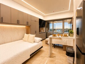 Ein modernes Schlafzimmer mit einem Bett, einem Tisch mit Tassen und einer Pflanze, einem großen Fenster und einem Kühlschrank.