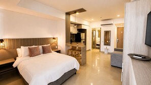 Ein modernes Hotelzimmer mit einem großen Bett, einem Schreibtisch, einem Sessel, einem Fernseher und einem durchgegangenen Tür erkennbaren Badezimmer.