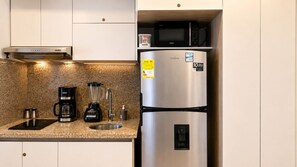 Eine Küche mit integriertem Mikrowellenherd, einer Kaffeemaschine, einem Mixer und einem Edelstahl-Kühlschrank.