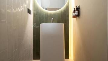Une salle de bain moderne avec un miroir rond, un lavabo cylindrique et un mur recouvert de carreaux verts.