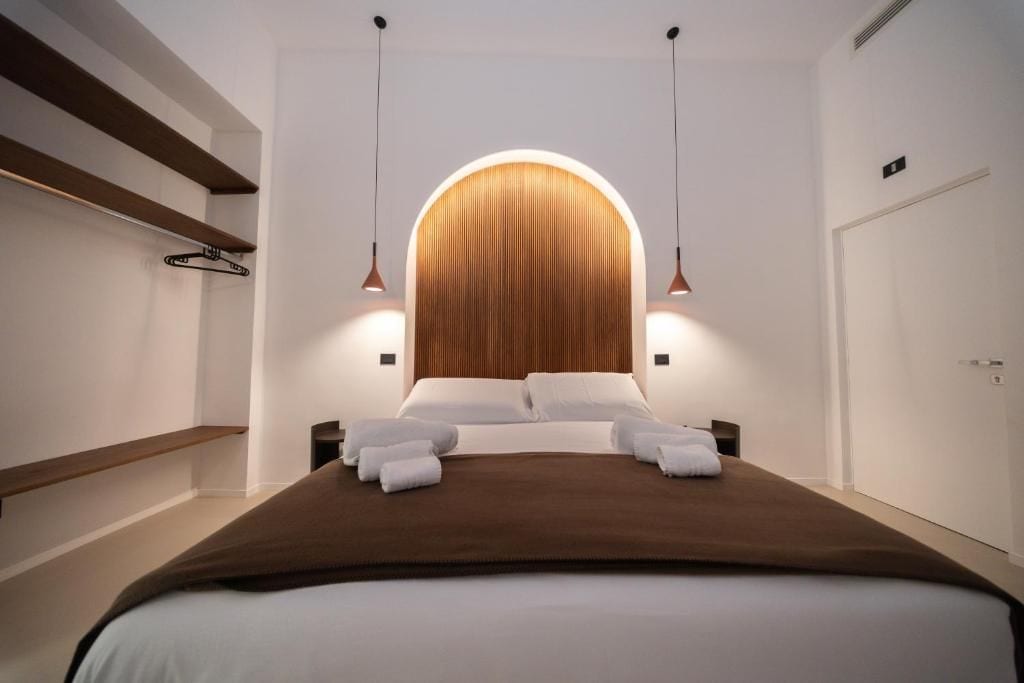 Une chambre d’hôtel moderne avec un grand lit, une tête de lit en bois et des luminaires suspendus.