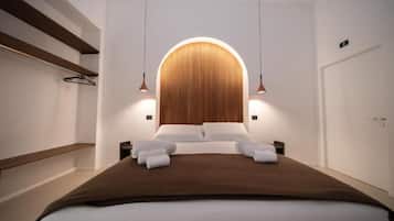 Une chambre d’hôtel moderne avec un grand lit, une tête de lit en bois et des luminaires suspendus.