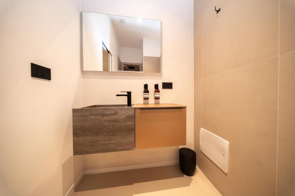 Un baño moderno con un espejo grande, un lavamanos y un cubo de basura.