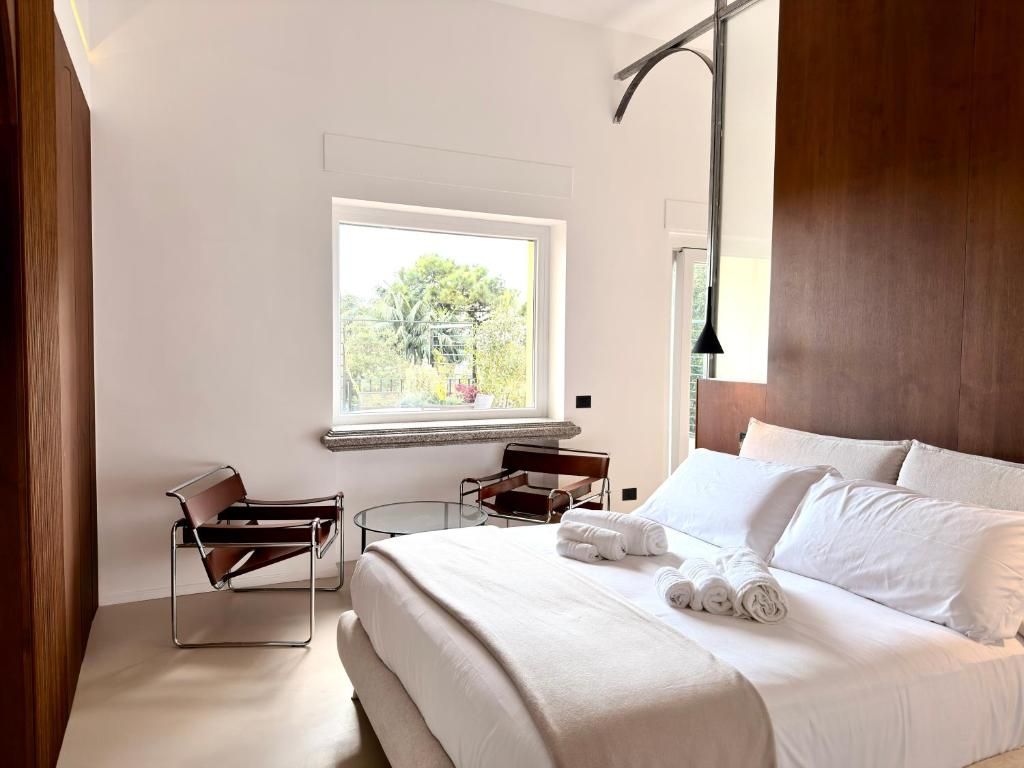 Una camera d'albergo con un letto, una finestra vista verde, una sedia e una lampada.