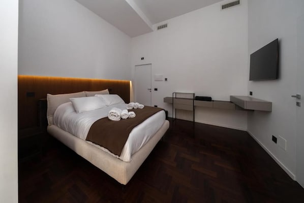 A modern hotel room with a large bed, a bedside table, a flat-screen TV, and a built-in desk.