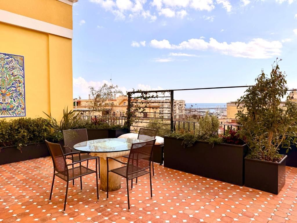 Una terrazza con un tavolo e sedie in vetro, circondata da piante in vaso e un pavimento piastrellato.