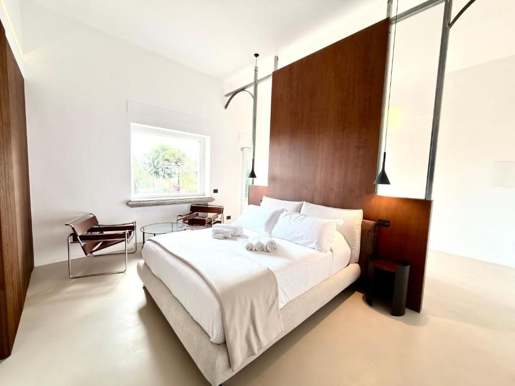 Une chambre moderne avec un grand lit, une table de chevet, une chaise et une fenêtre.