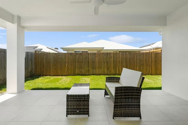 Une terrasse extérieure dotée d’un ventilateur de plafond, de deux fauteuils en osier et d’une petite table.